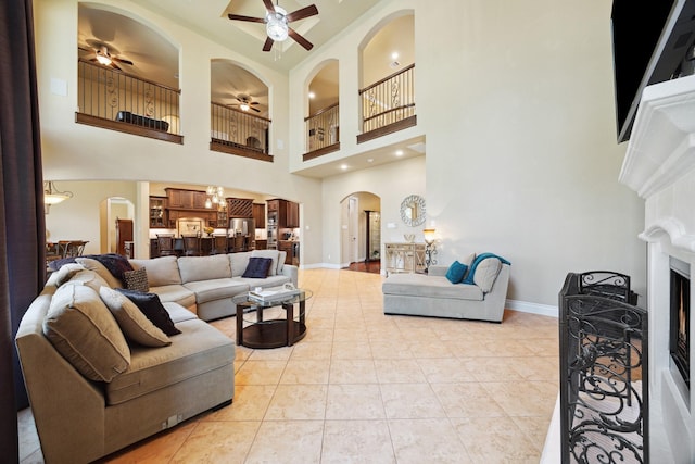 living room with a ceiling fan, arched walkways, a fireplace, light tile patterned floors, and baseboards