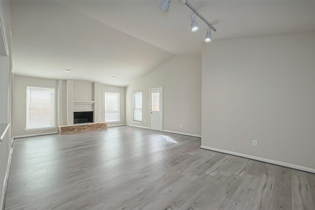 unfurnished living room featuring plenty of natural light, a large fireplace, lofted ceiling, and wood finished floors