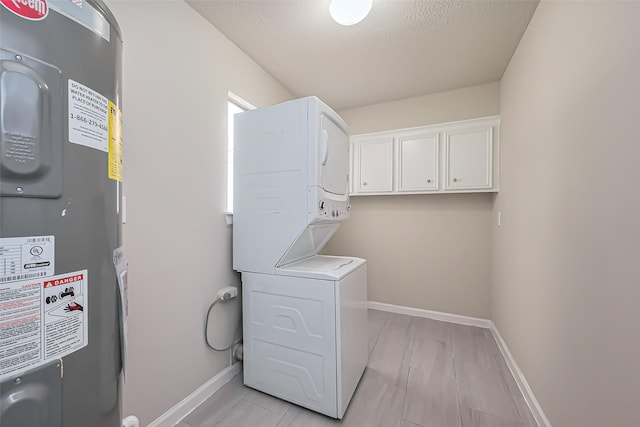 laundry area with laundry area, electric water heater, stacked washer / drying machine, and baseboards