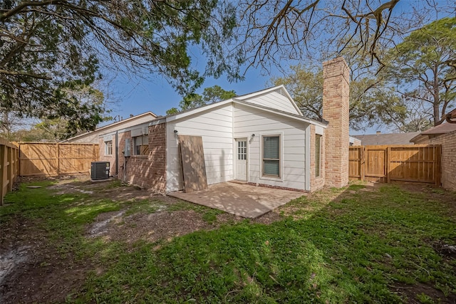 rear view of house featuring a lawn, central AC, a fenced backyard, a chimney, and a patio area