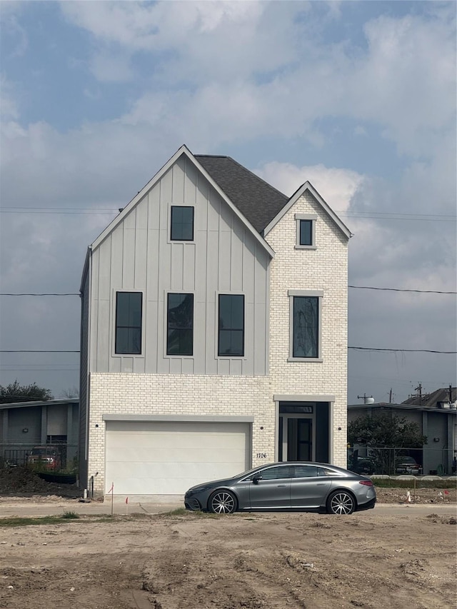 view of front facade featuring brick siding, board and batten siding, an attached garage, and a shingled roof