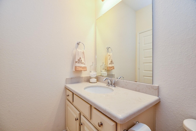 bathroom with vanity, toilet, and a textured wall