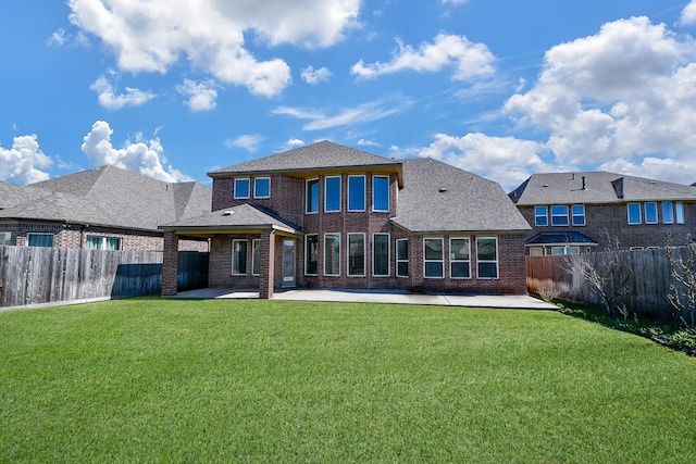 rear view of house with brick siding, roof with shingles, a lawn, a fenced backyard, and a patio