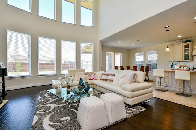 living area with hardwood / wood-style flooring, recessed lighting, baseboards, and a towering ceiling