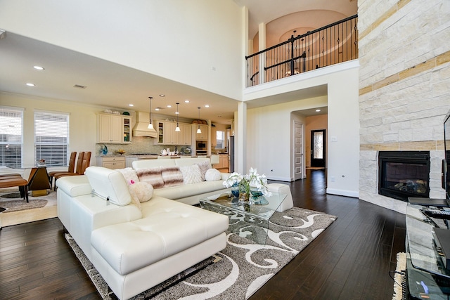 living area featuring baseboards, a stone fireplace, recessed lighting, a towering ceiling, and dark wood-style floors