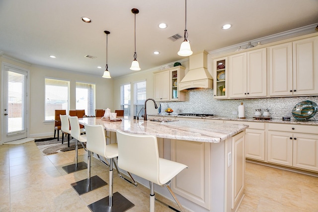 kitchen with premium range hood, visible vents, a breakfast bar, a sink, and decorative backsplash