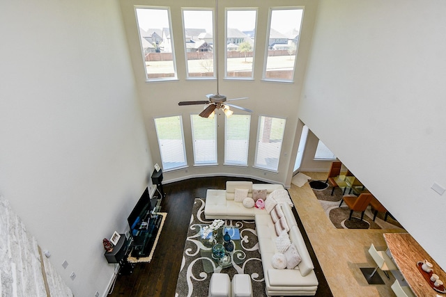 living area with baseboards, wood finished floors, and a towering ceiling