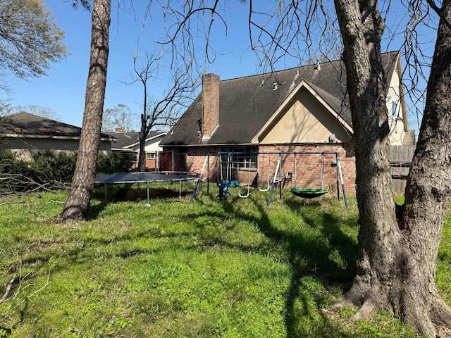 back of house featuring brick siding, a yard, a chimney, and a trampoline