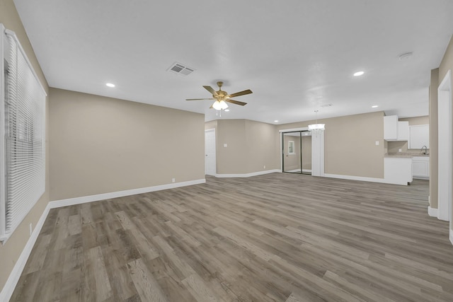 unfurnished living room with light wood finished floors, visible vents, baseboards, ceiling fan with notable chandelier, and recessed lighting