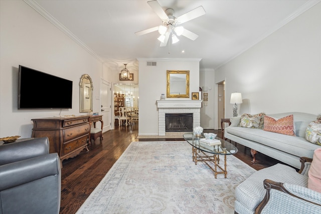 living room featuring visible vents, a brick fireplace, ornamental molding, ceiling fan with notable chandelier, and wood finished floors