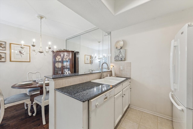 kitchen featuring white appliances, an inviting chandelier, a peninsula, a sink, and decorative light fixtures