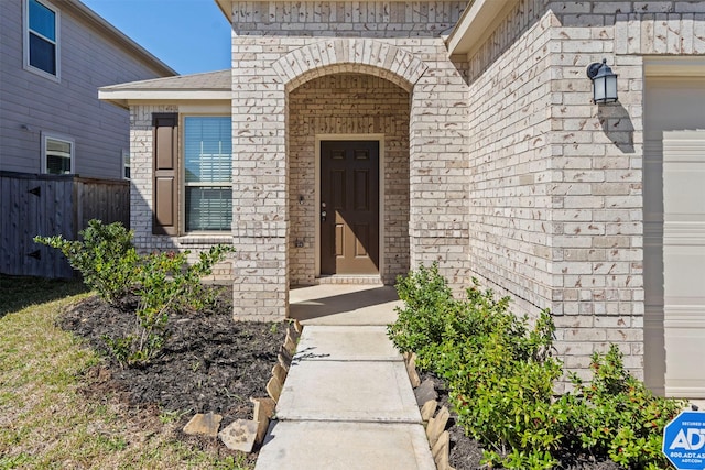 view of exterior entry featuring fence, brick siding, and a shingled roof