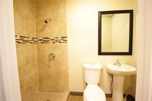 bathroom featuring a tile shower, toilet, baseboards, and a sink