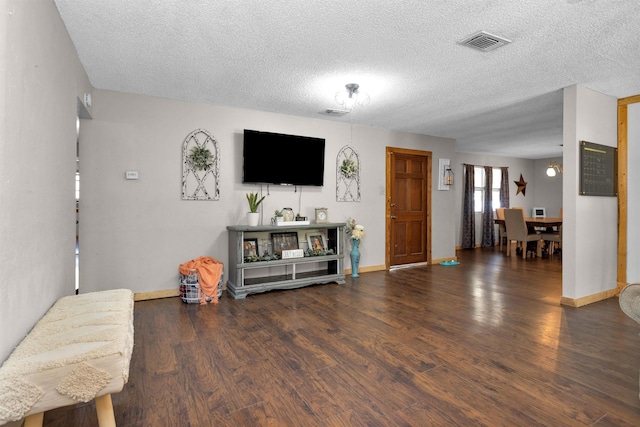 living room featuring visible vents, baseboards, a textured ceiling, and wood finished floors