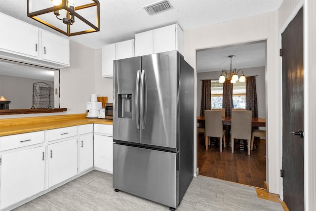 kitchen featuring visible vents, a notable chandelier, a textured ceiling, white cabinets, and stainless steel fridge with ice dispenser