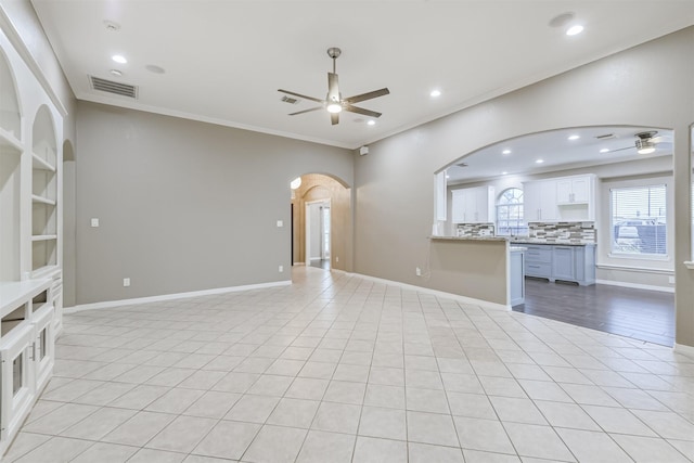 unfurnished living room featuring arched walkways, visible vents, a ceiling fan, and ornamental molding