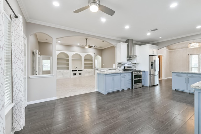 kitchen with dark wood-style floors, ceiling fan, stainless steel appliances, and wall chimney range hood