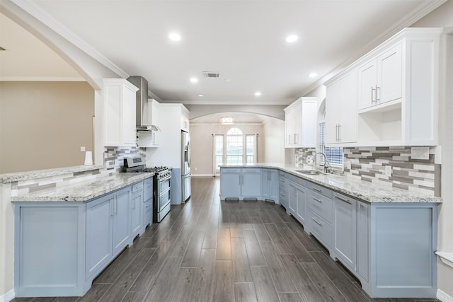 kitchen featuring visible vents, a sink, appliances with stainless steel finishes, a peninsula, and wall chimney range hood