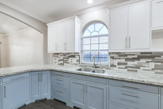 kitchen featuring light stone countertops, a sink, white cabinetry, crown molding, and backsplash