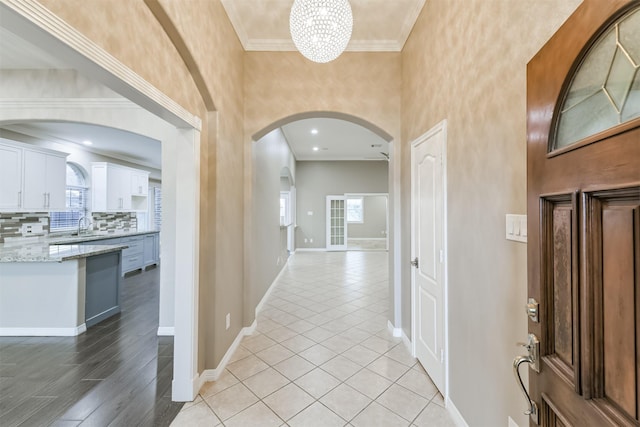 entrance foyer featuring light tile patterned floors, baseboards, an inviting chandelier, arched walkways, and crown molding