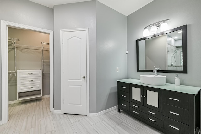 bathroom with a shower, baseboards, vanity, and a spacious closet