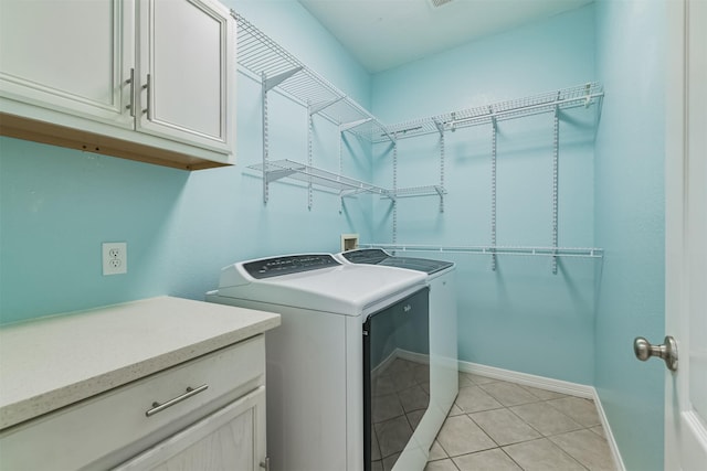 clothes washing area featuring light tile patterned floors, washing machine and dryer, cabinet space, and baseboards