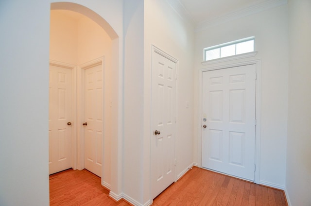 entrance foyer with arched walkways, crown molding, and light wood-style floors