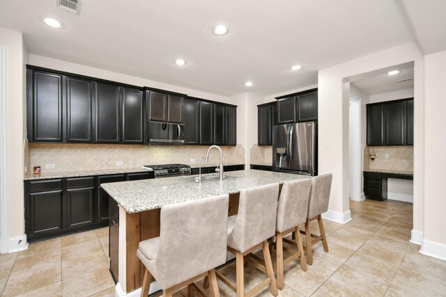 kitchen with visible vents, light stone countertops, appliances with stainless steel finishes, dark cabinetry, and a sink