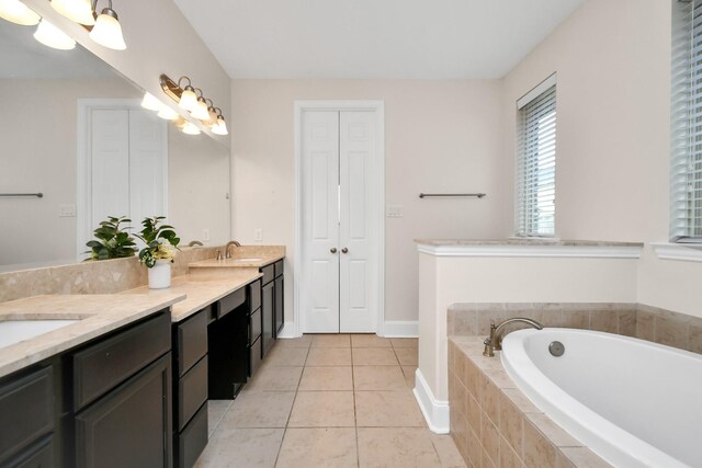 bathroom with a garden tub, baseboards, double vanity, a sink, and tile patterned floors