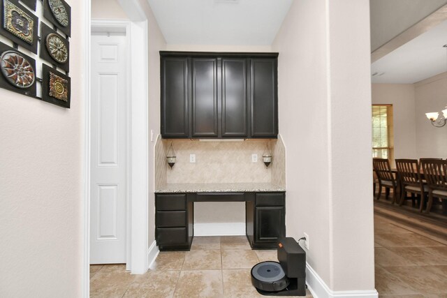 interior space featuring tasteful backsplash, light stone countertops, a chandelier, dark cabinetry, and light tile patterned flooring