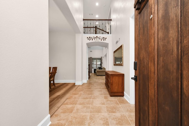 foyer entrance featuring baseboards, light tile patterned floors, recessed lighting, a towering ceiling, and arched walkways