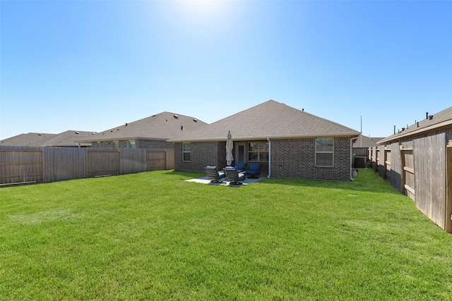 rear view of house with a lawn, a patio, a fenced backyard, a shingled roof, and brick siding