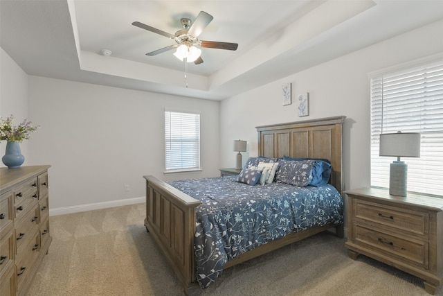 bedroom featuring a tray ceiling, light carpet, baseboards, and a ceiling fan