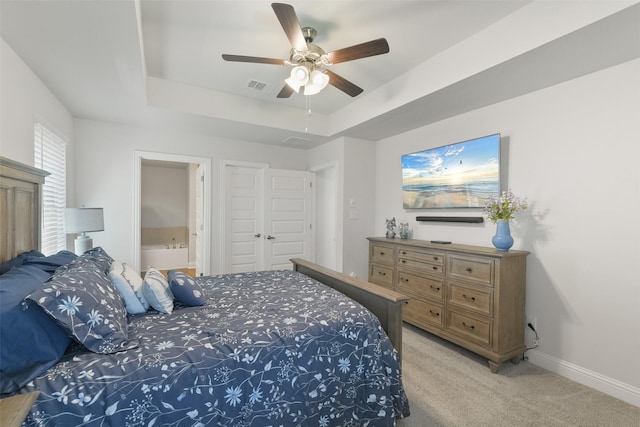 bedroom with visible vents, baseboards, light colored carpet, a tray ceiling, and ensuite bath