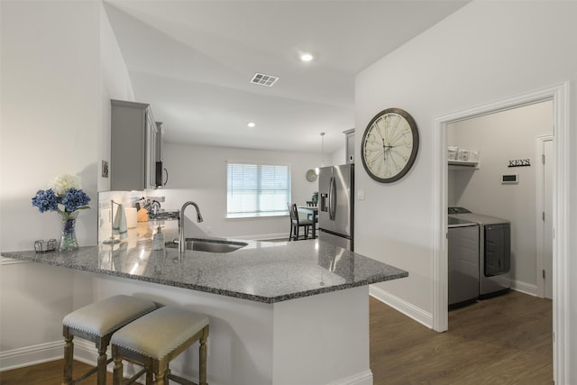 kitchen featuring visible vents, dark stone countertops, stainless steel refrigerator with ice dispenser, independent washer and dryer, and a sink