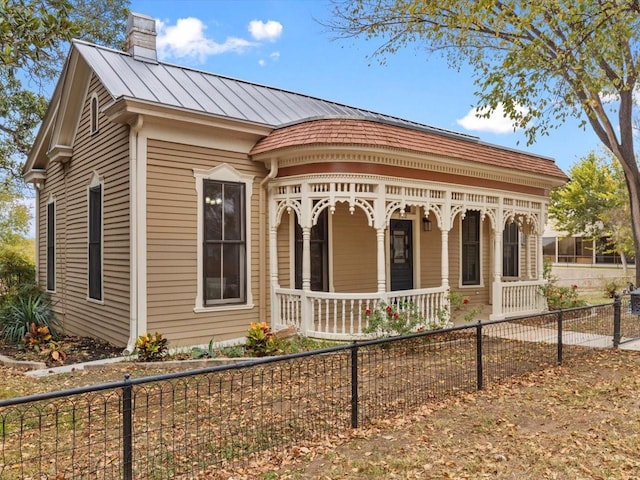 view of front facade with a fenced front yard, covered porch, a chimney, metal roof, and a standing seam roof