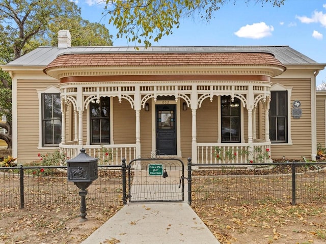 view of front of property featuring a fenced front yard, covered porch, a chimney, and a gate