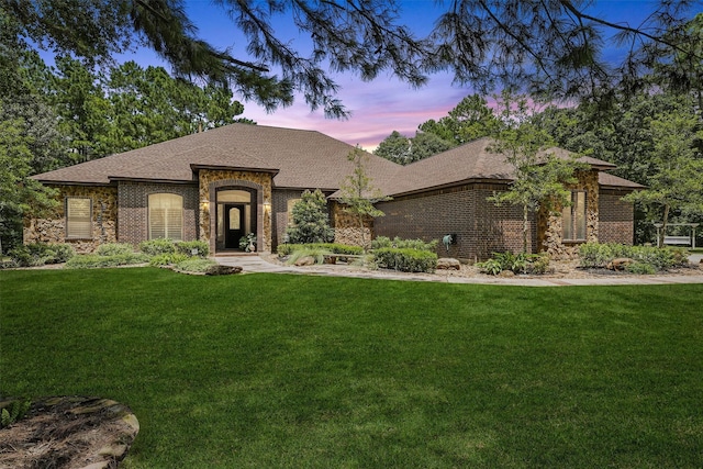 view of front of house featuring brick siding, a lawn, and a shingled roof