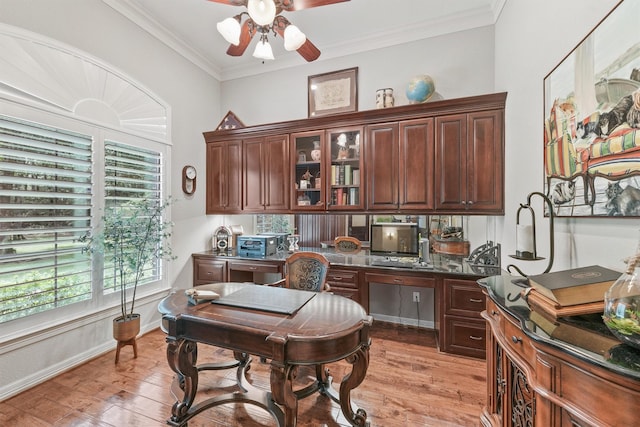 office with crown molding, baseboards, light wood-type flooring, built in desk, and a ceiling fan