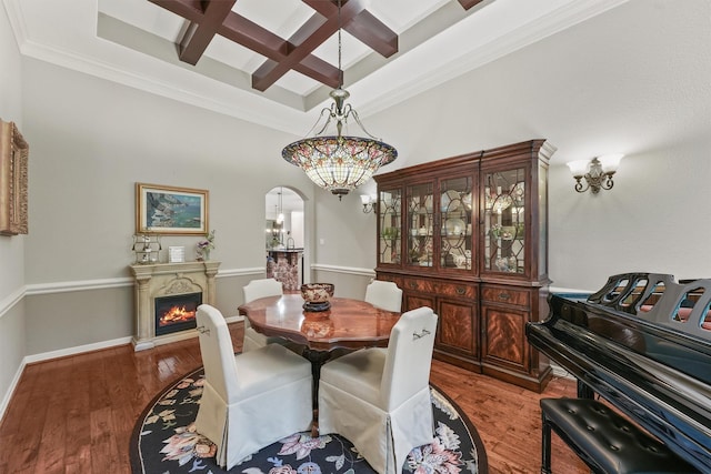 dining room with a chandelier, a warm lit fireplace, wood finished floors, arched walkways, and coffered ceiling