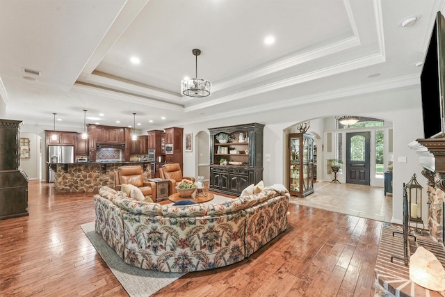 living room featuring a raised ceiling, arched walkways, a chandelier, and light wood finished floors