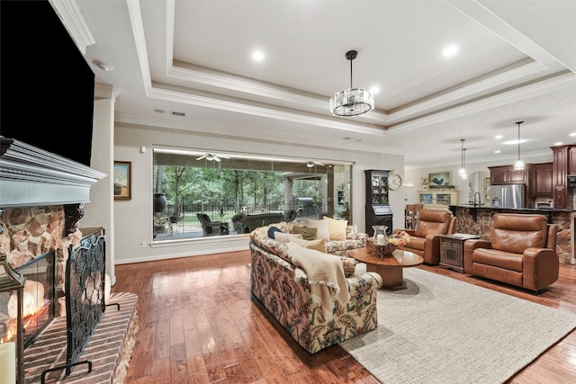 living area with crown molding, a warm lit fireplace, a raised ceiling, and hardwood / wood-style flooring