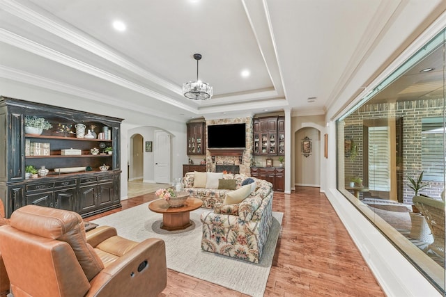 living room with light wood finished floors, a tray ceiling, arched walkways, crown molding, and a fireplace