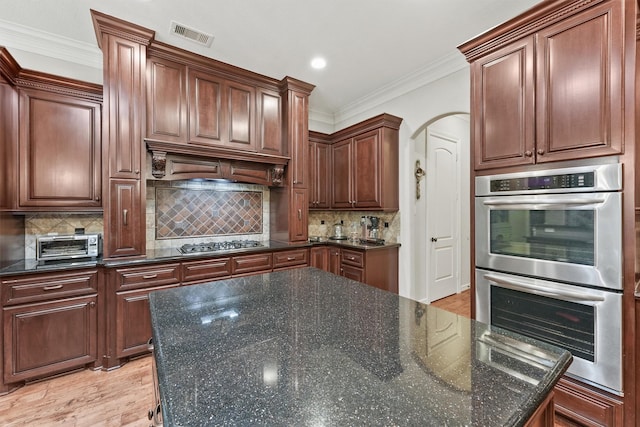 kitchen featuring light wood finished floors, arched walkways, ornamental molding, stainless steel appliances, and backsplash