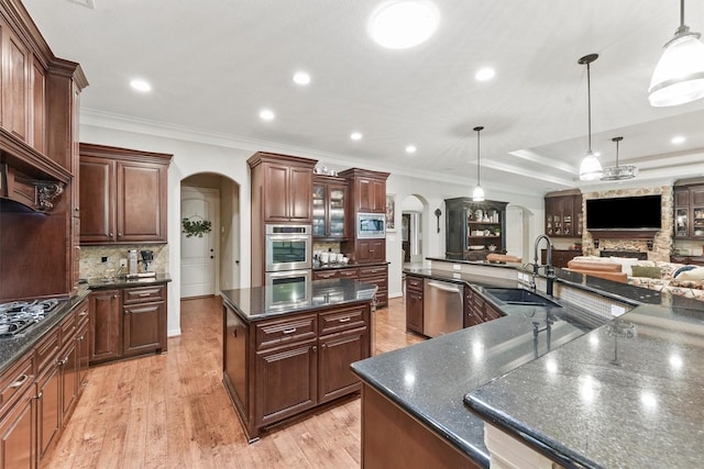 kitchen featuring a large island, ornamental molding, a sink, arched walkways, and appliances with stainless steel finishes