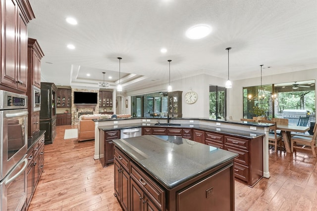 kitchen with open floor plan, a tray ceiling, a fireplace, a large island, and a sink