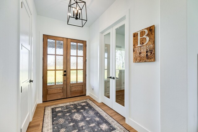 doorway to outside with light wood-style flooring, french doors, an inviting chandelier, and baseboards