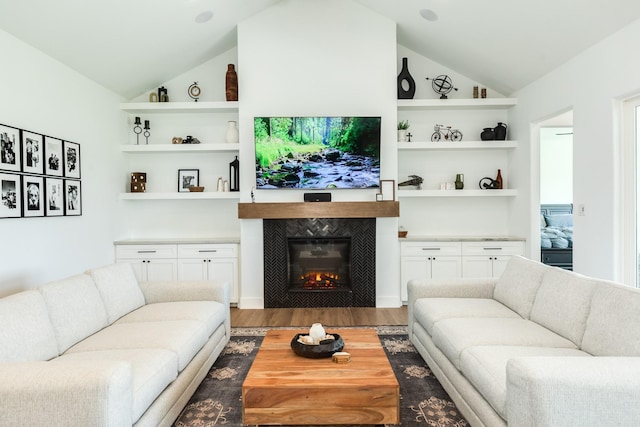 living area with a tile fireplace, built in shelves, light wood-style floors, and vaulted ceiling