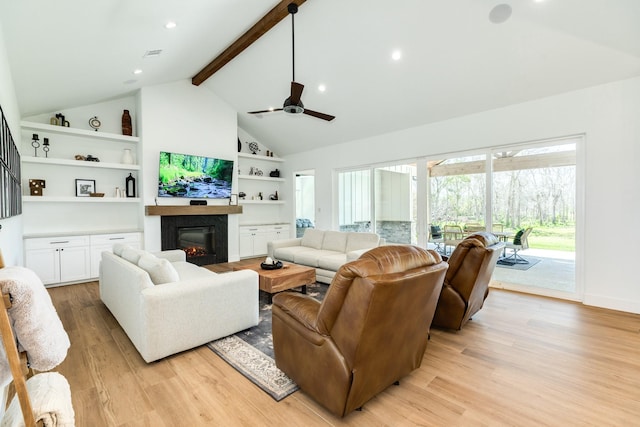 living area with built in features, high vaulted ceiling, a glass covered fireplace, beamed ceiling, and light wood-type flooring