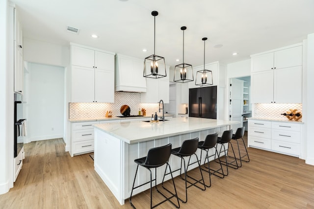 kitchen featuring visible vents, light wood-style floors, custom exhaust hood, black appliances, and a sink